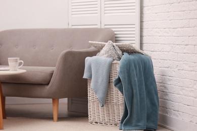Photo of Basket with blankets and pillow near sofa indoors