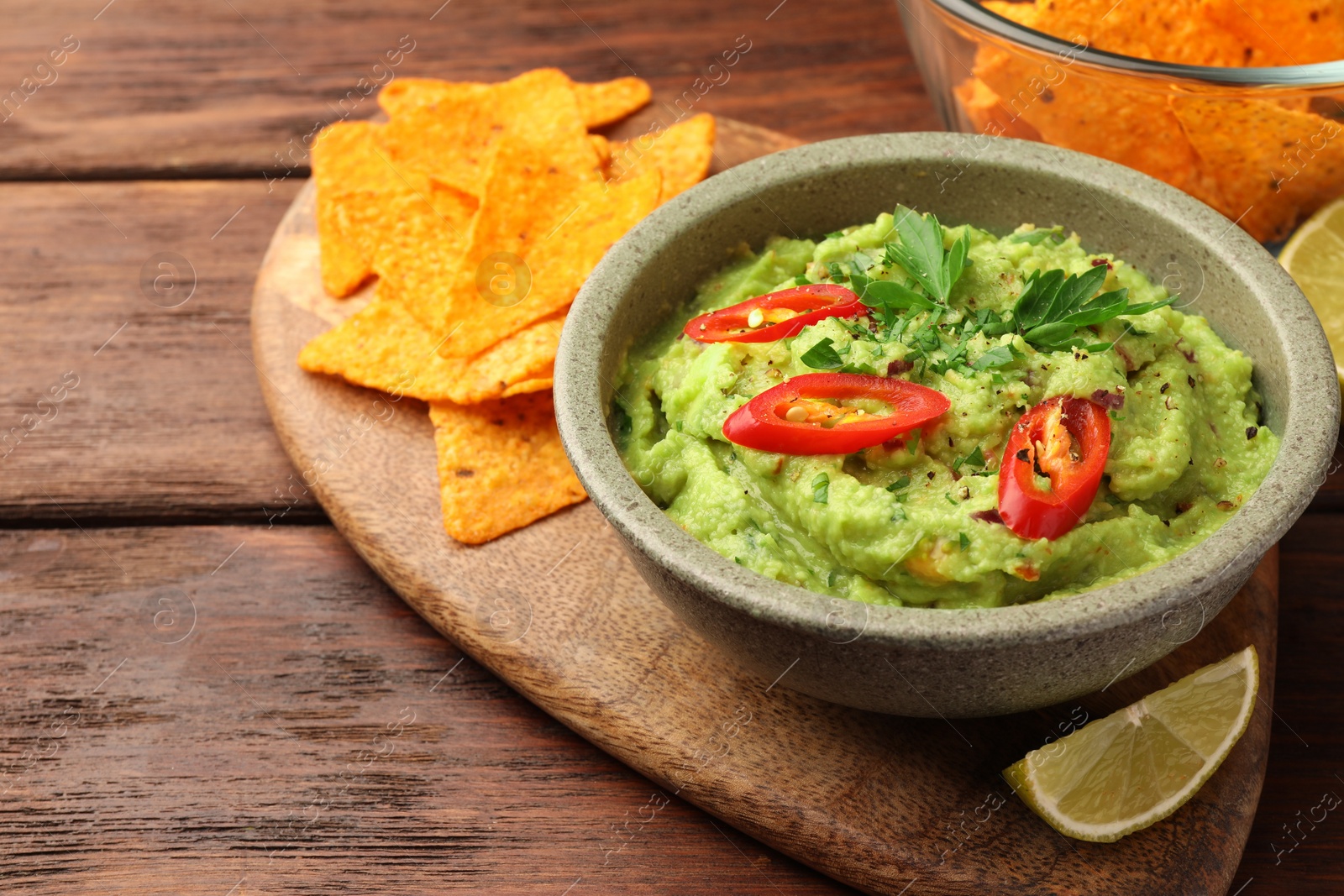 Photo of Bowl of delicious guacamole, lime and tortilla chips on wooden table, closeup. Space for text