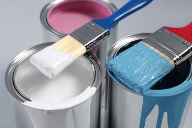 Cans of paints and brushes on light blue background, closeup