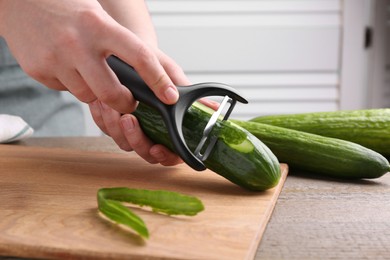 Photo of Woman peeling cucumber at wooden table indoors, closeup