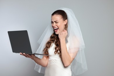 Excited bride with laptop on gray background