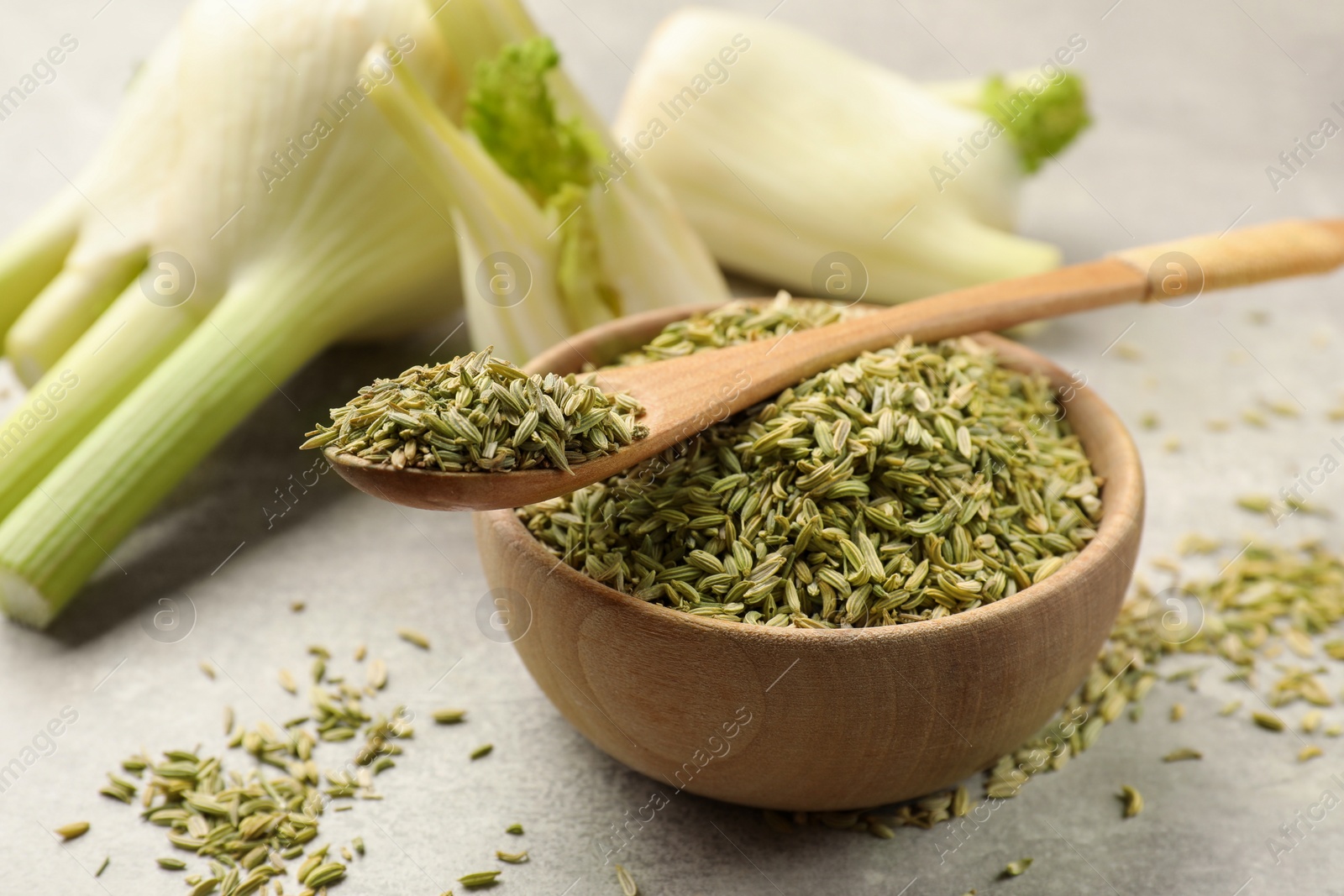 Photo of Fresh fennel bulbs, bowl and spoon with seeds on light gray table, closeup