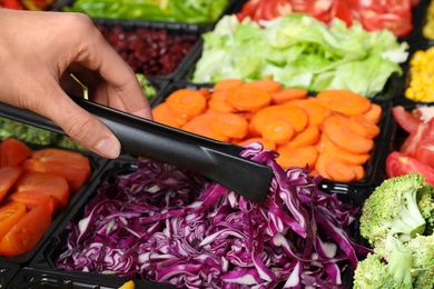 Young woman taking chopped red cabbage from salad bar, closeup