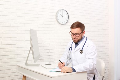 Pediatrician with clipboard working at table in clinic