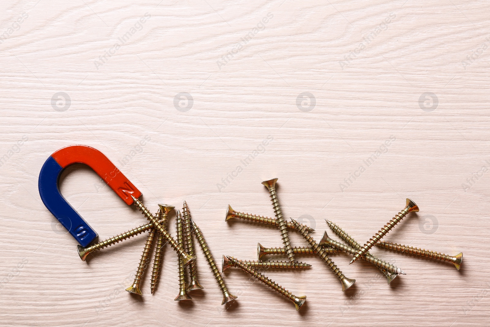 Photo of Magnet attracting screws on light wooden background, flat lay. Space for text