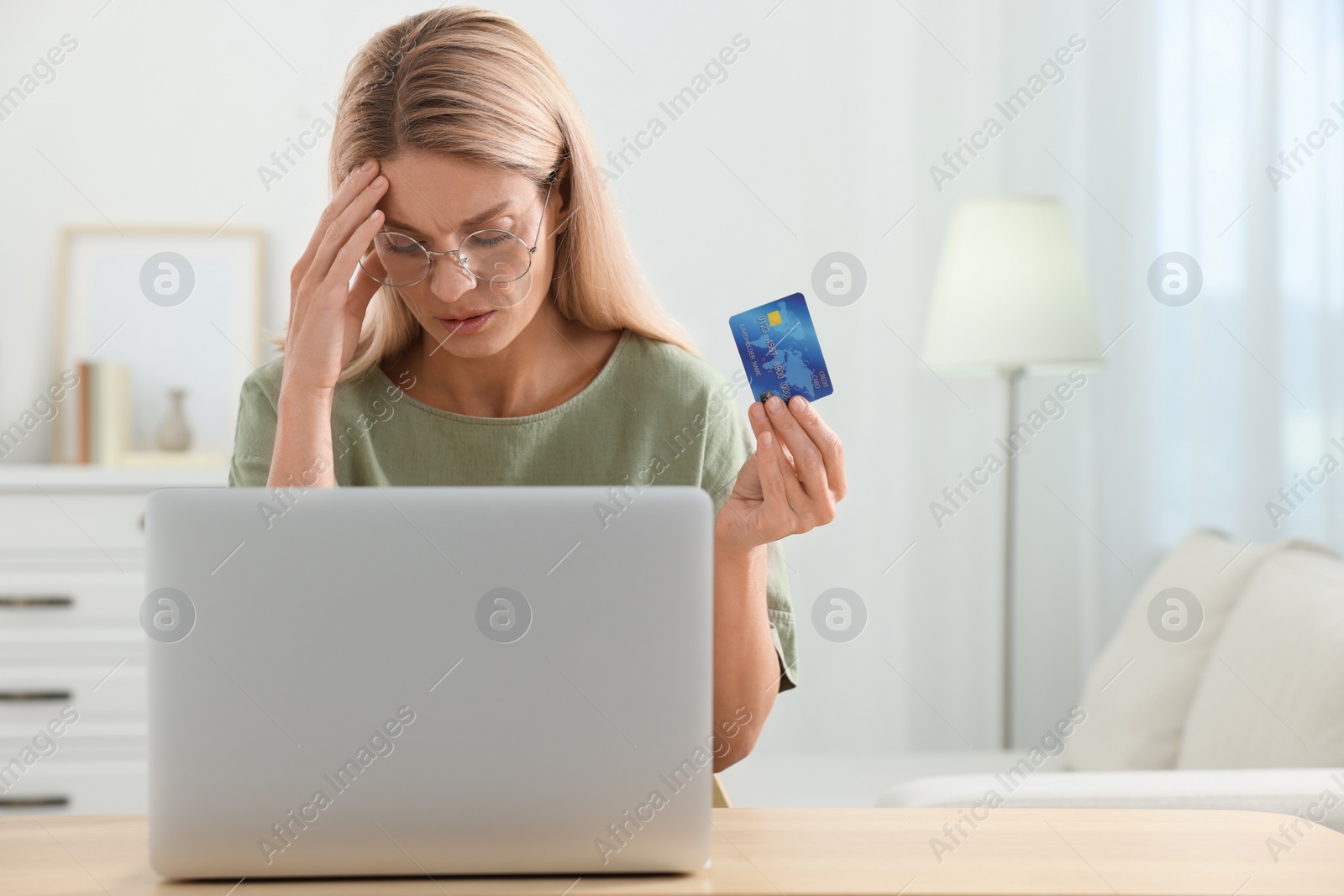 Photo of Stressed woman with credit card using laptop at home, space for text. Be careful - fraud