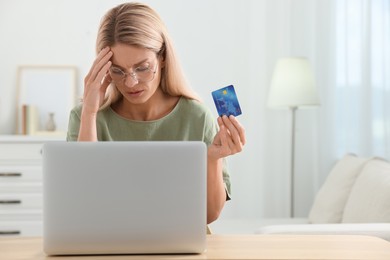 Stressed woman with credit card using laptop at home, space for text. Be careful - fraud