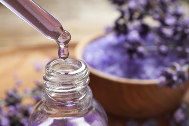 Natural oil dripping into bottle and lavender flowers on table, closeup with space for text. Cosmetic product