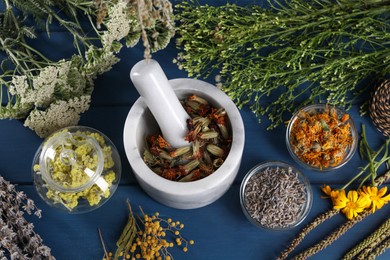 Photo of Mortar with pestle and many different herbs on blue wooden table, flat lay