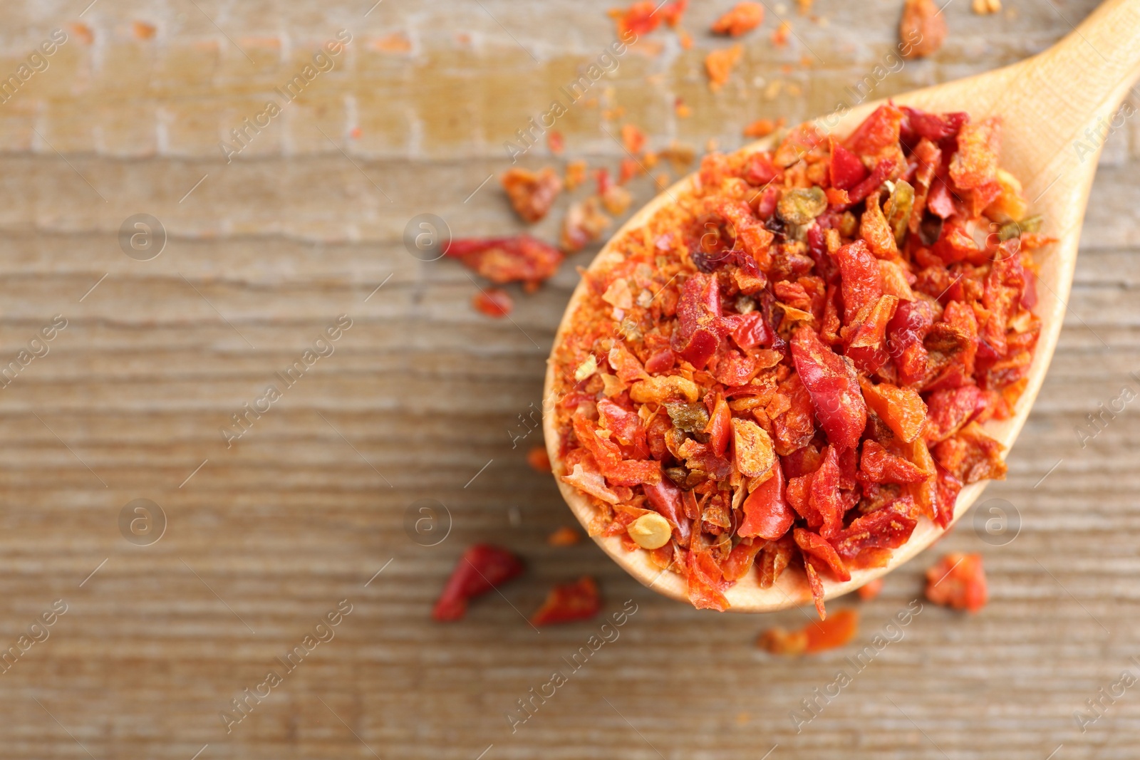 Photo of Aromatic spice. Red chili pepper flakes in spoon on wooden table, top view. Space for text