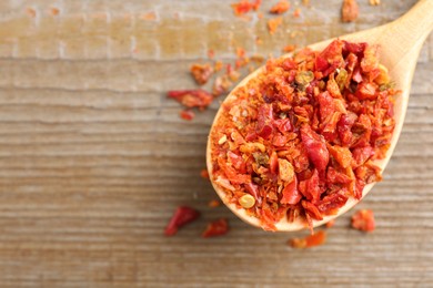 Photo of Aromatic spice. Red chili pepper flakes in spoon on wooden table, top view. Space for text