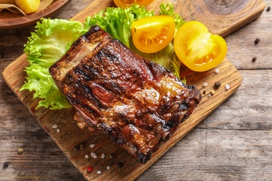 Photo of Board with barbecued ribs and garnish on wooden background, top view