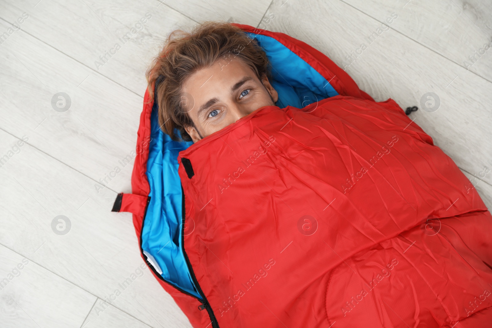 Photo of Young man in comfortable sleeping bag on floor, top view