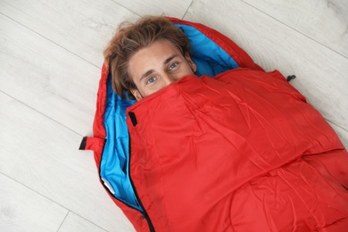 Young man in comfortable sleeping bag on floor, top view