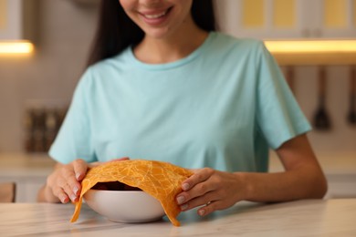 Photo of Woman packing bowl into beeswax food wrap at light table in kitchen, closeup