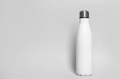 Stylish white thermo bottle with water drops on light grey background, space for text