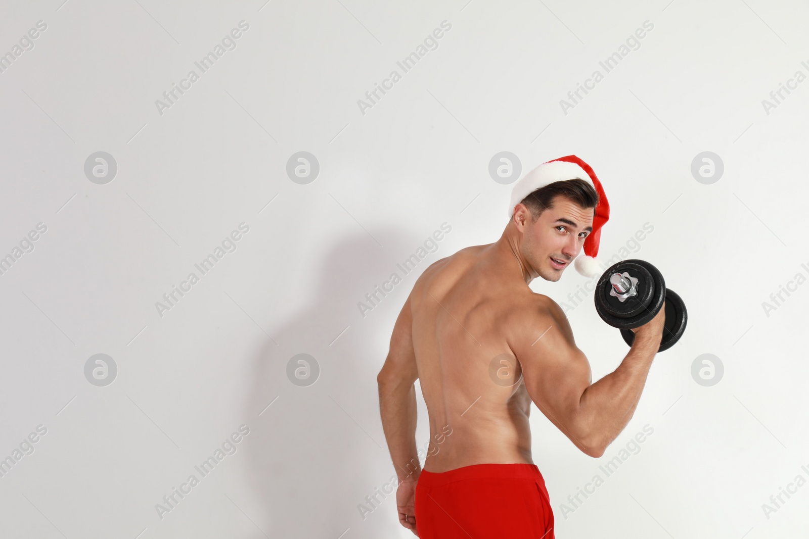 Photo of Sexy shirtless Santa Claus with dumbbell on light background, space for text
