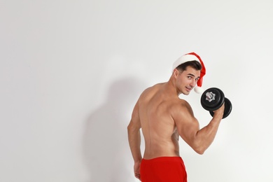 Sexy shirtless Santa Claus with dumbbell on light background, space for text