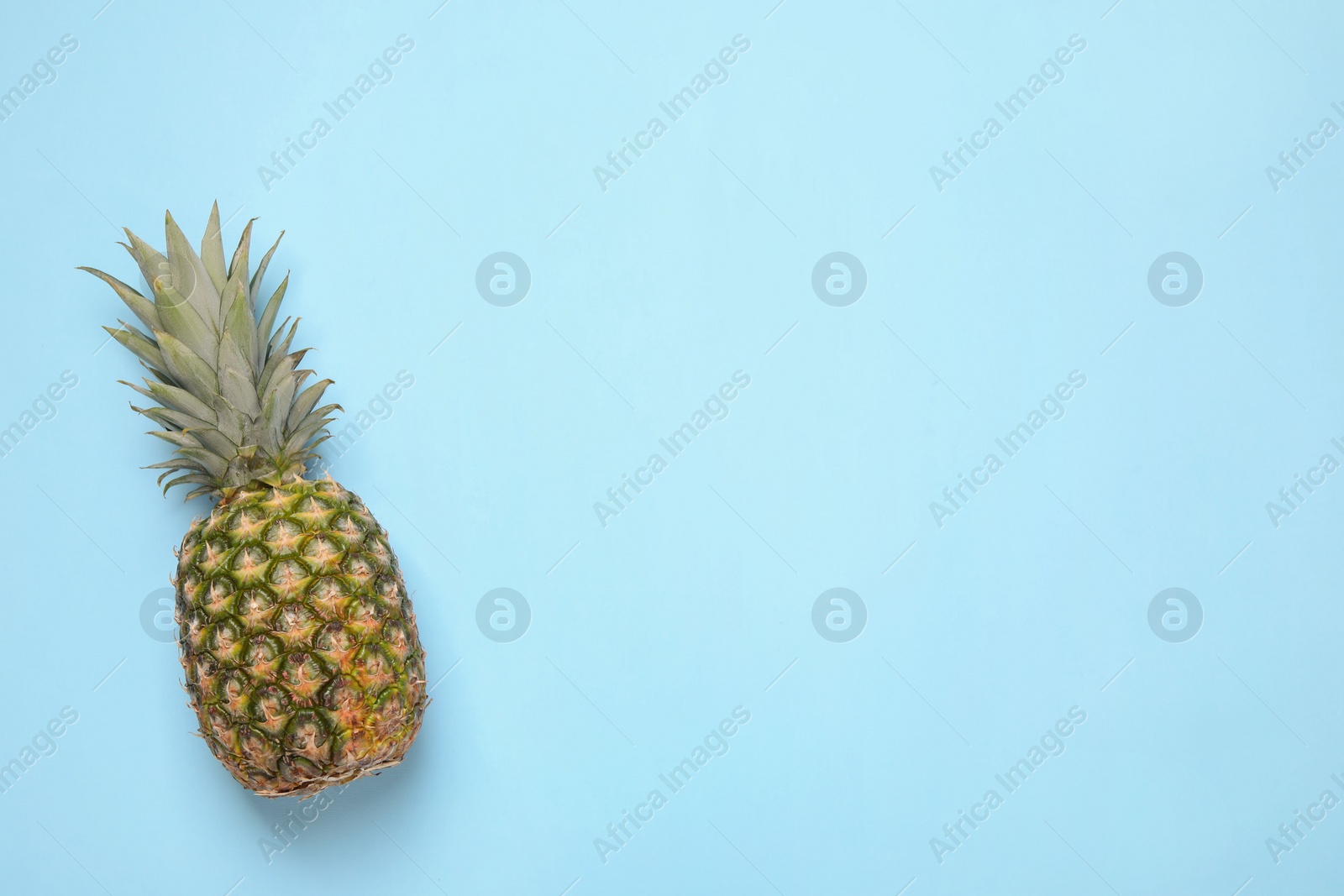 Photo of Whole ripe pineapple on light blue background, top view. Space for text