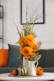 Beautiful autumn bouquets and pumpkins on coffee table near sofa in room