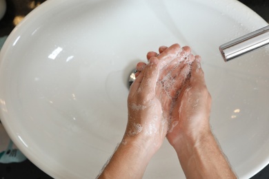 Man washing hands with soap over sink in bathroom, top view. Space for text