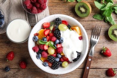 Photo of Fresh tasty fruit salad with yogurt on wooden table, flat lay