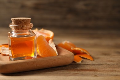 Photo of Bottle of tangerine essential oil and peeled fresh fruit on wooden table. Space for text