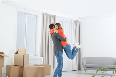 Happy couple hugging near moving boxes in their new house