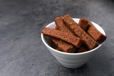 Photo of Crispy rusks in bowl on grey table, closeup
