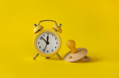 Photo of Alarm clock and baby dummy on yellow background. Time to give birth
