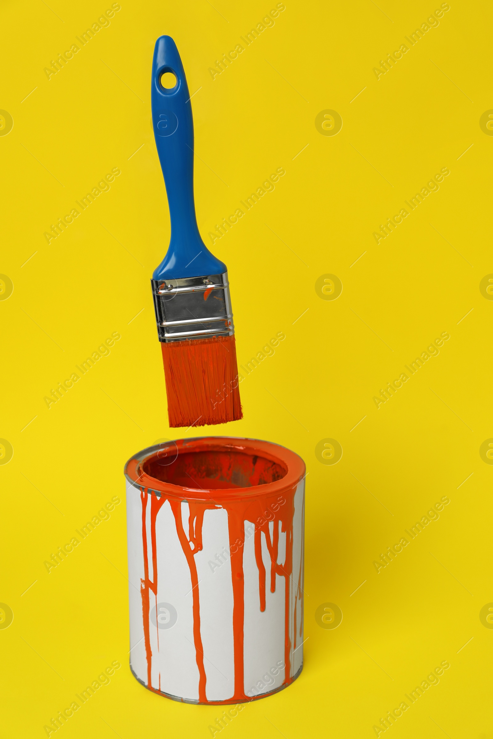 Photo of Can of orange paint and brush on yellow background