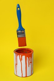 Photo of Can of orange paint and brush on yellow background