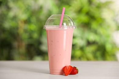 Photo of Plastic cup of tasty smoothie and fresh strawberries on wooden table outdoors