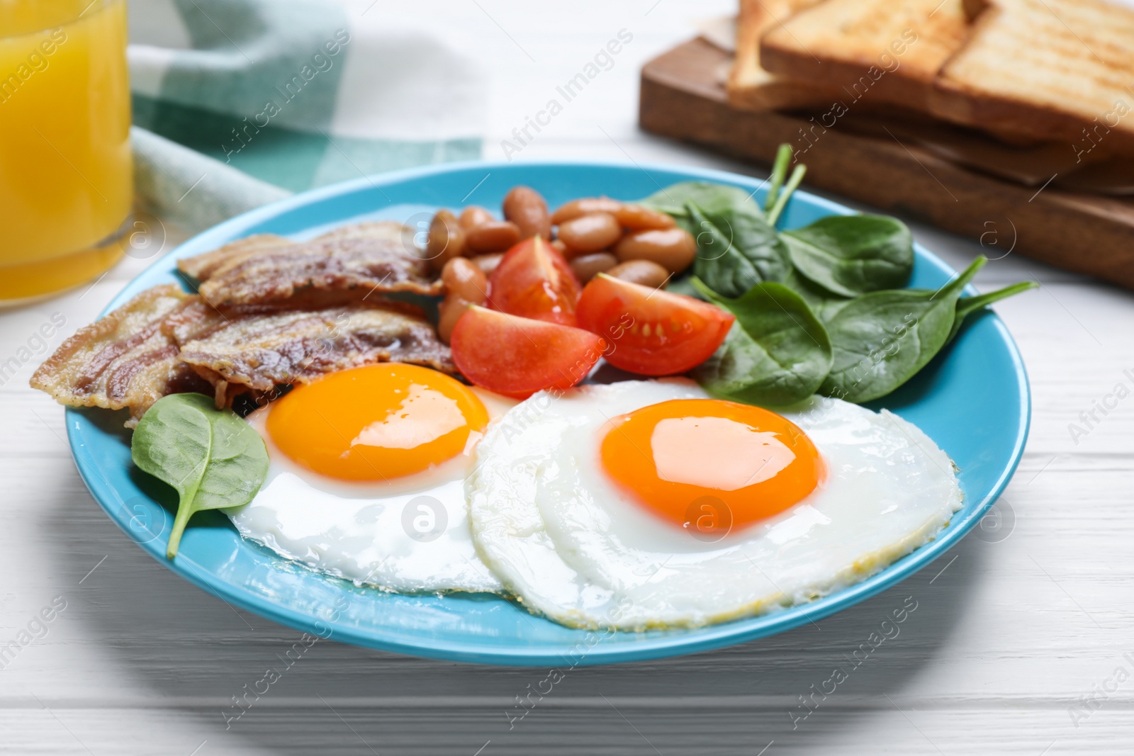 Photo of Tasty breakfast with fried eggs, bacon and spinach served on white wooden table, closeup