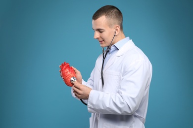 Young man in white coat with heart model on color model