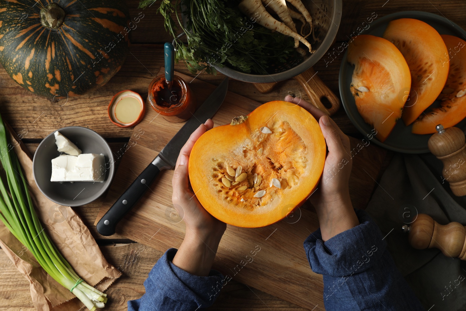 Photo of Woman with cut fresh ripe pumpkin at wooden table, top view