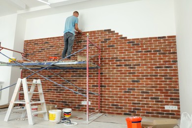 Photo of Professional builder gluing decorative bricks on wall in room. Tiles installation process