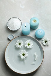 Photo of Bowl with water and flowers, burning candles, sea salt on grey marble floor, flat lay. Pedicure procedure