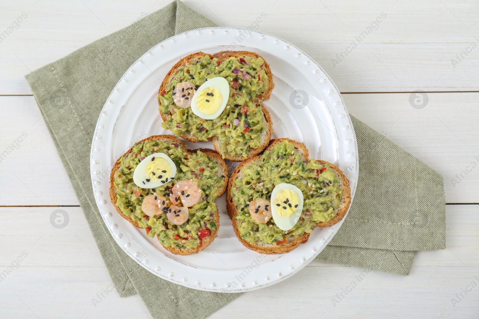 Photo of Slices of bread with tasty guacamole, eggs and shrimp on white wooden table, top view