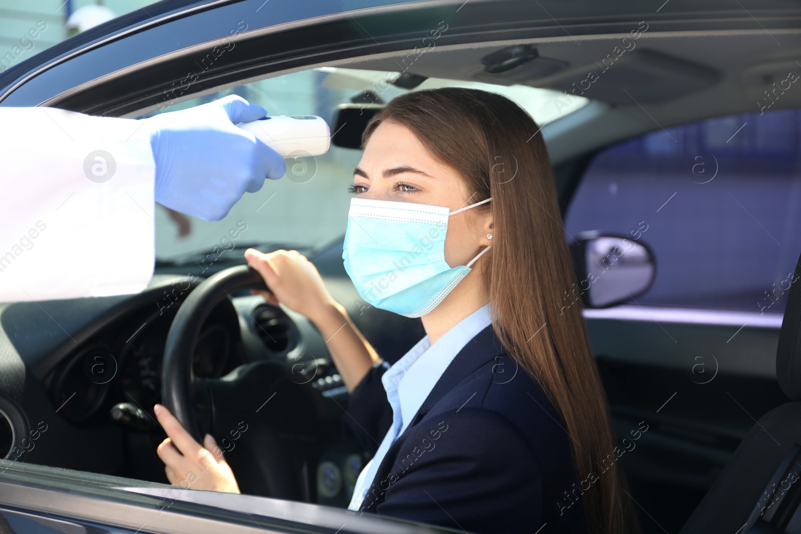 Photo of Doctor measuring woman's temperature with non contact infrared thermometer in car