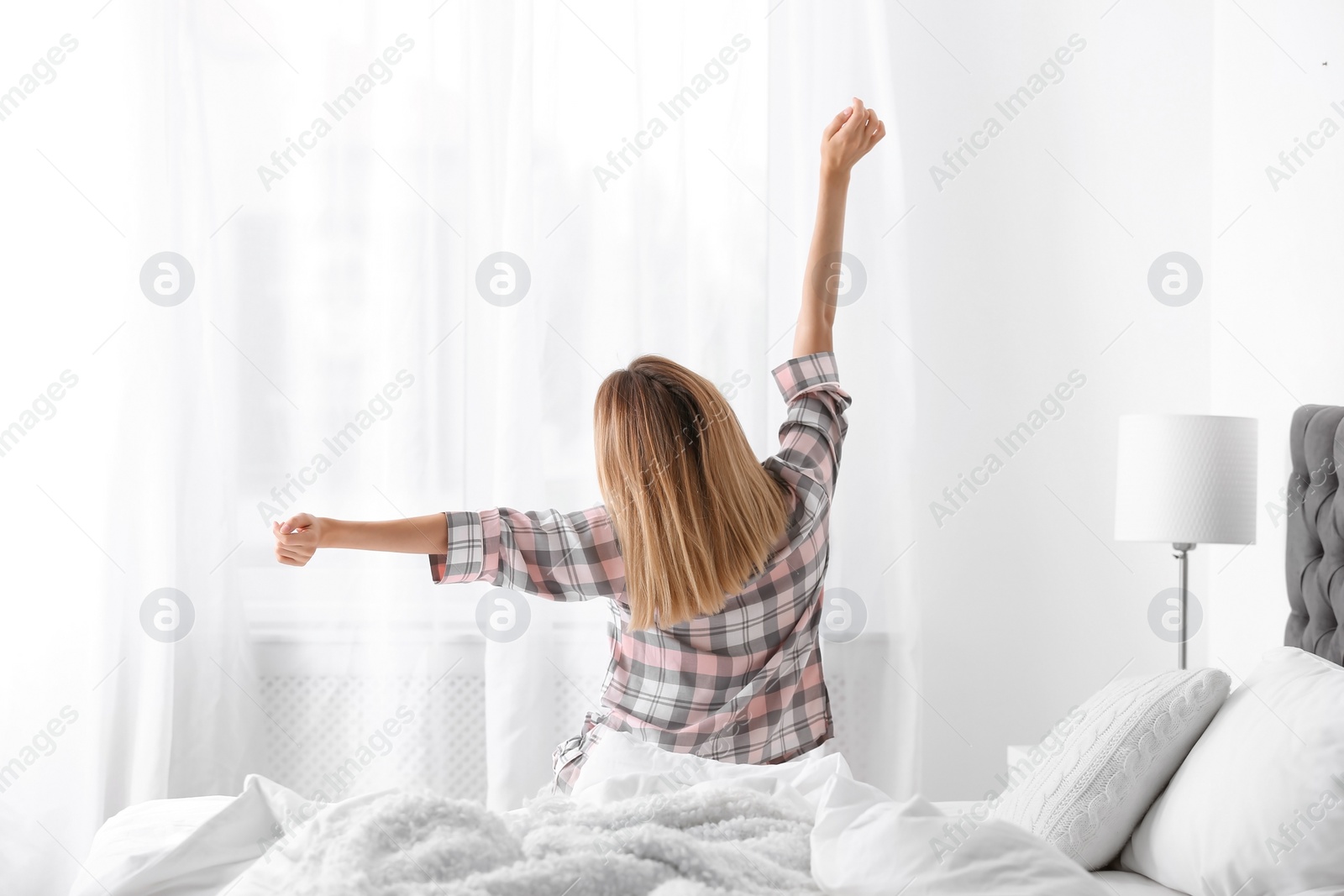 Photo of Young beautiful woman stretching after sleeping on bed at home
