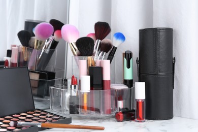 Photo of Bright lip glosses among different cosmetic products on white dressing table