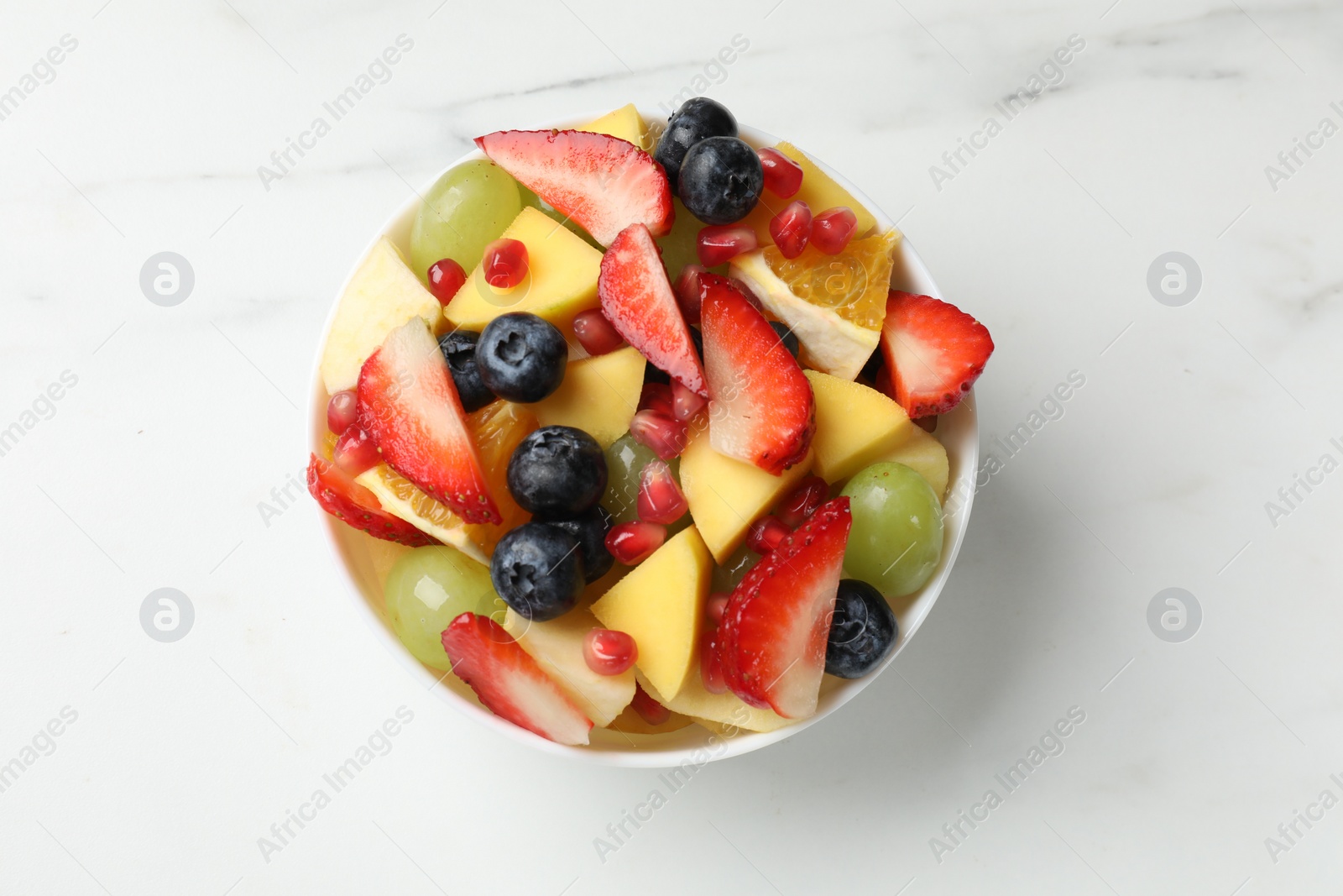 Photo of Tasty fruit salad in bowl on white table, top view
