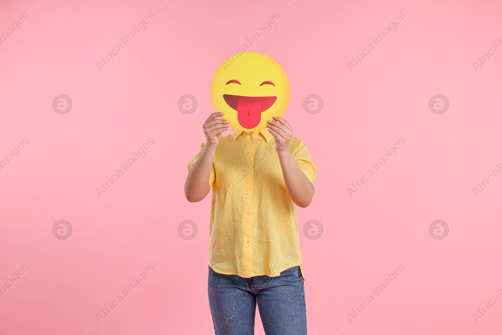 Photo of Woman covering face with emoticon sticking out tongue on pink background