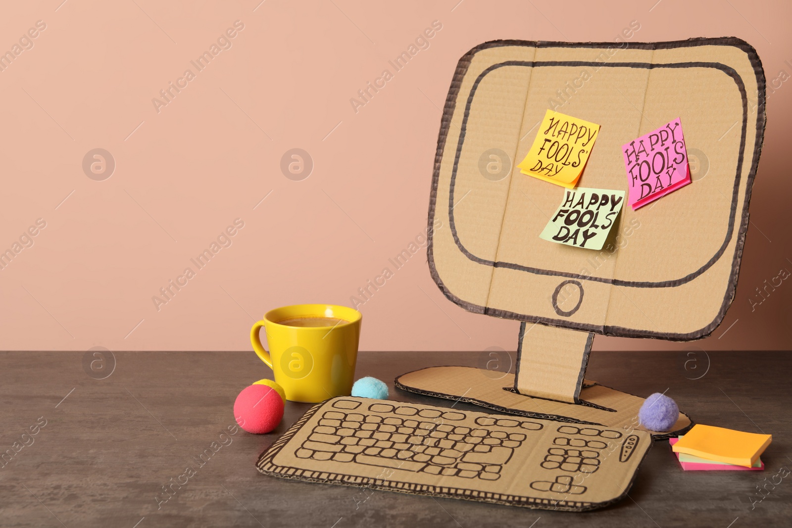 Photo of Cardboard computer with Happy Fools' Day notes and cup on wooden table. Space for text