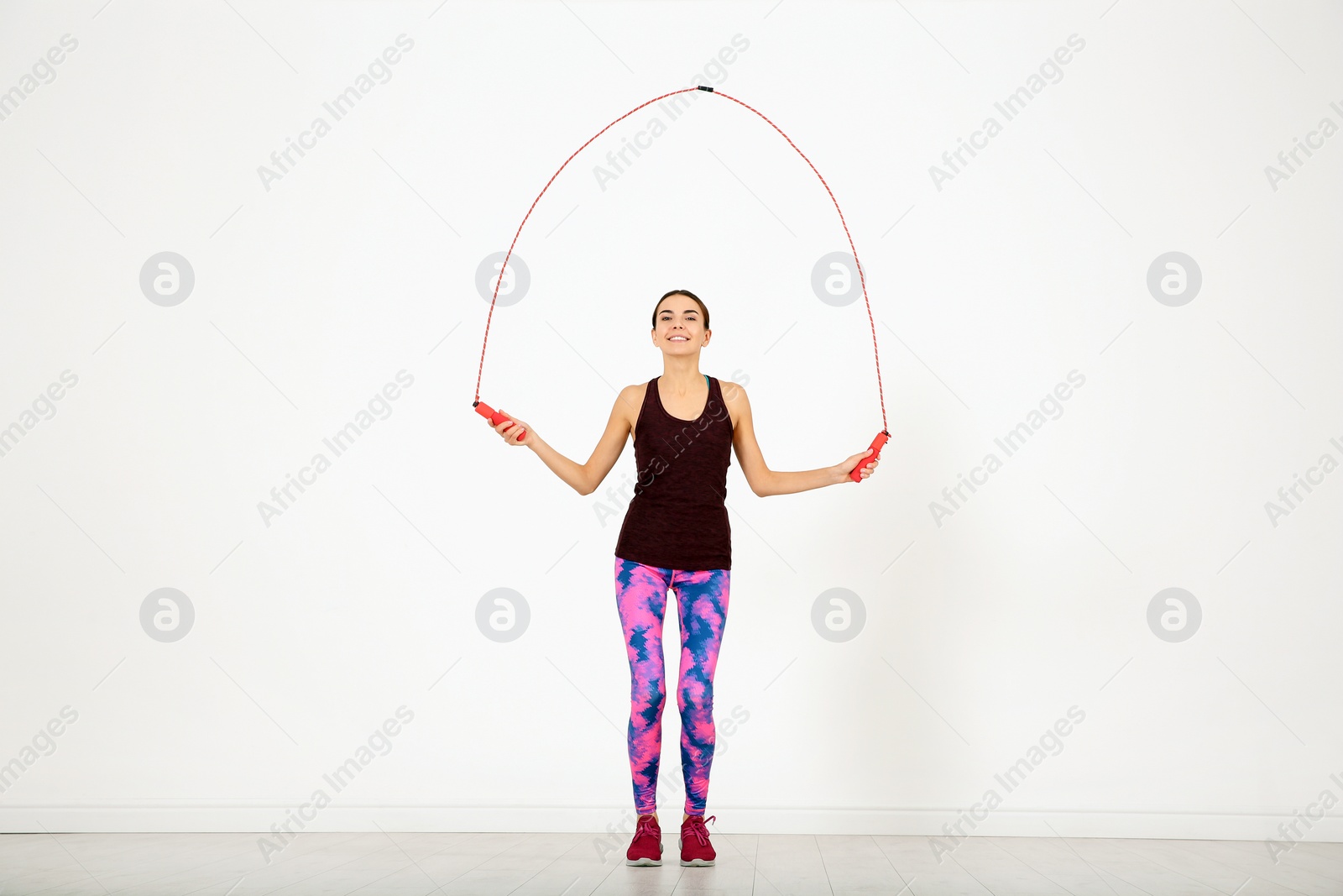 Photo of Full length portrait of young sportive woman training with jump rope in light room