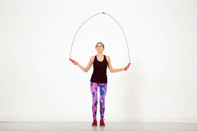 Full length portrait of young sportive woman training with jump rope in light room