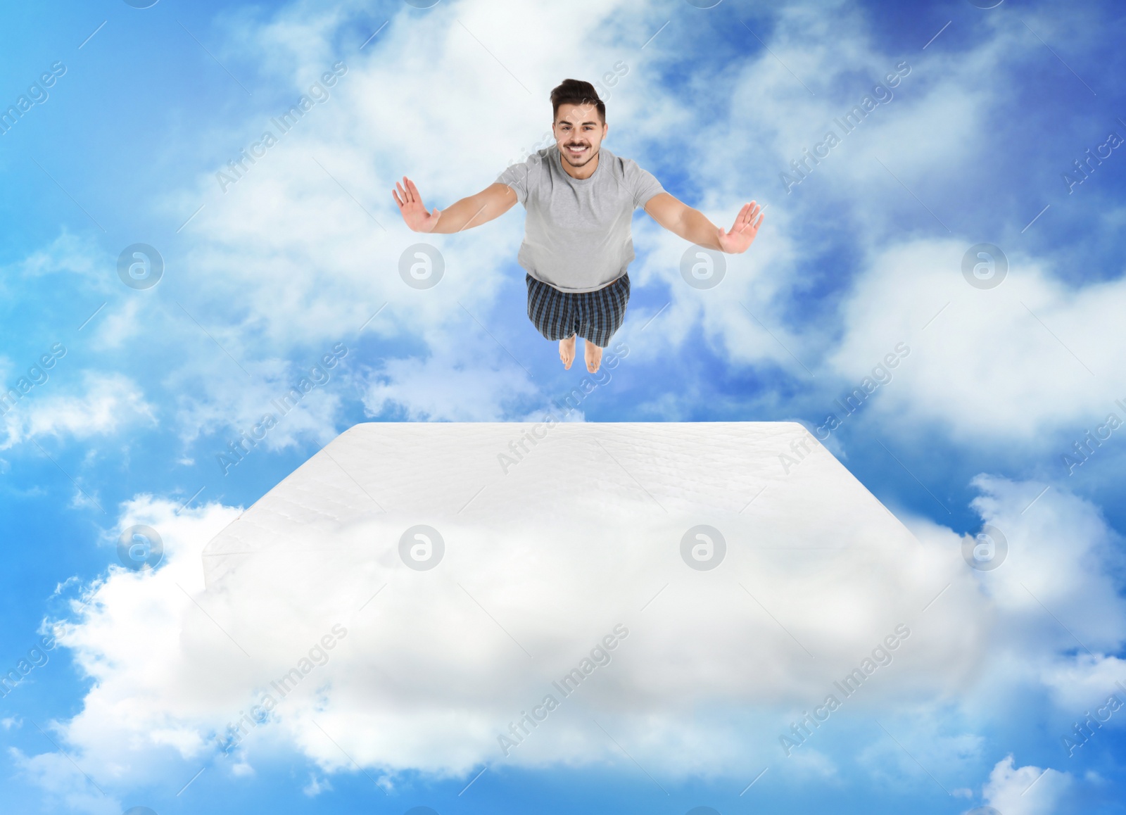 Image of Young man jumping on mattress in clouds