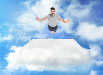 Image of Young man jumping on mattress in clouds