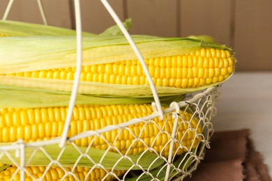 Tasty fresh corn cobs in metal basket on white wooden table, closeup